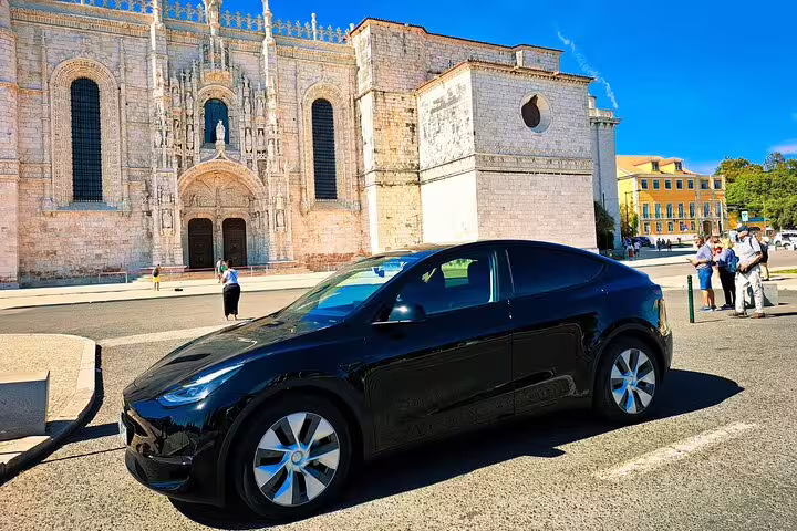 Sleek black car in front of Lisbon's historic Jerónimos Monastery, offering private transfer service to Algarve.