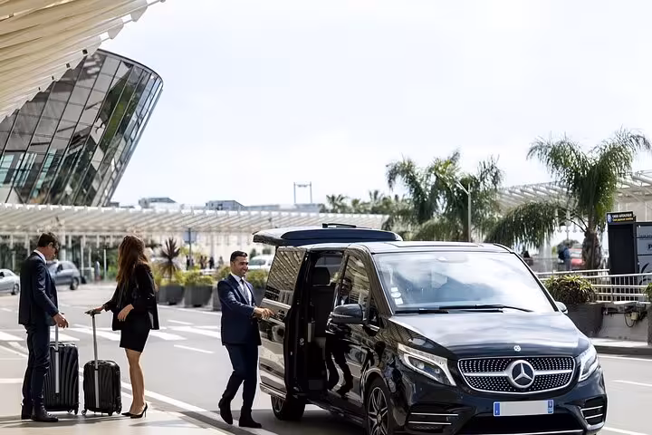 Chauffeur opening door of black Mercedes van for two passengers at airport departure zone
