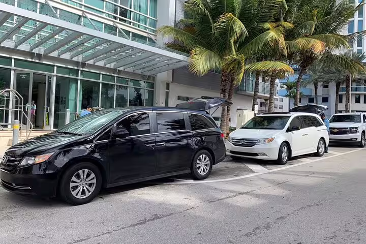 Black and white Honda Odyssey minivans parked outside a modern hotel entrance with palm trees