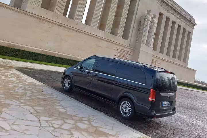 Black Mercedes-Benz V-Class van parked in front of a neoclassical memorial building in Normandy