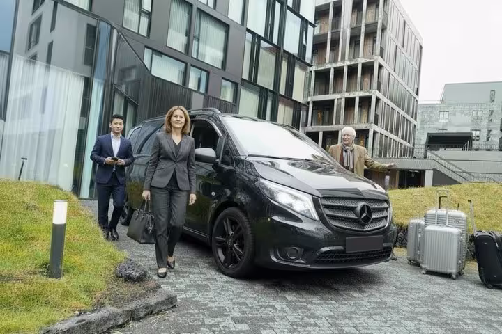 Passengers with luggage boarding a black Mercedes van for private transfer at Reykjavik hotel
