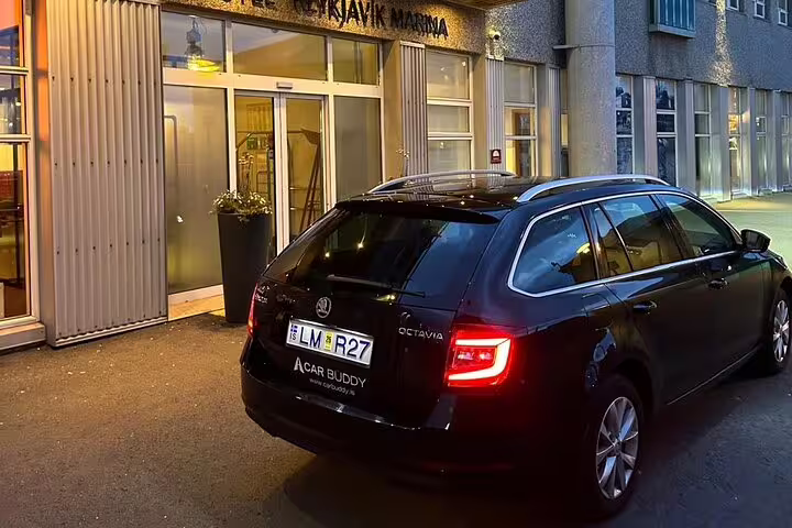Black Skoda Octavia estate car parked outside Reykjavik Marina Hotel at dusk with Car Buddy branding