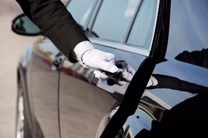 Professional driver in white gloves opening black car door for premium private transfer between Rome and Positano, Italy