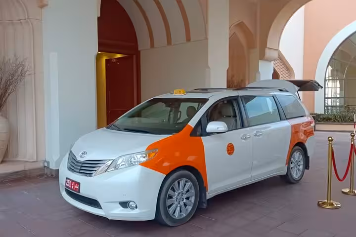 Modern white and orange taxi minivan waiting at Shangri-La resort entrance for private transfer to Muscat Airport