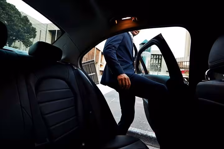 Businessman in suit stepping into a black luxury sedan for a private transfer service