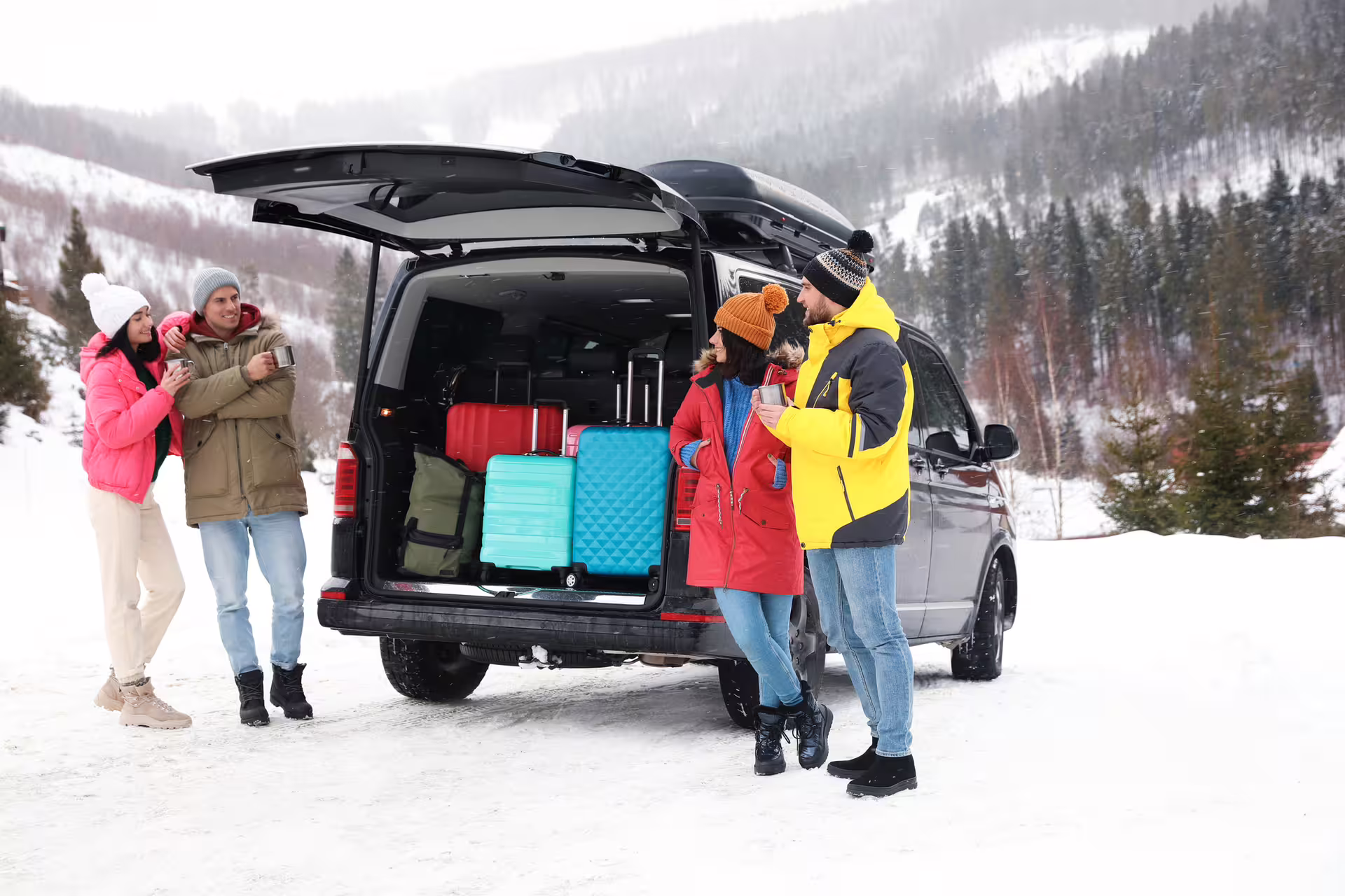 Group of four travelers with colorful luggage at open van trunk in snowy mountain landscape