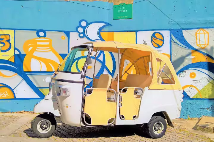 Vibrant tuk-tuk parked by colorful street art in Porto, perfect for exploring the city on a private half-day tour.