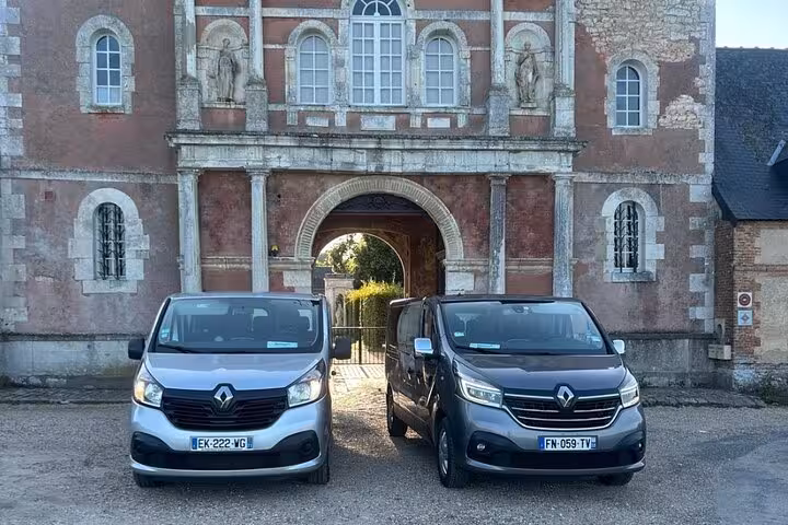 Two Renault vans parked in front of a historic French château gateway on a private Versailles tour