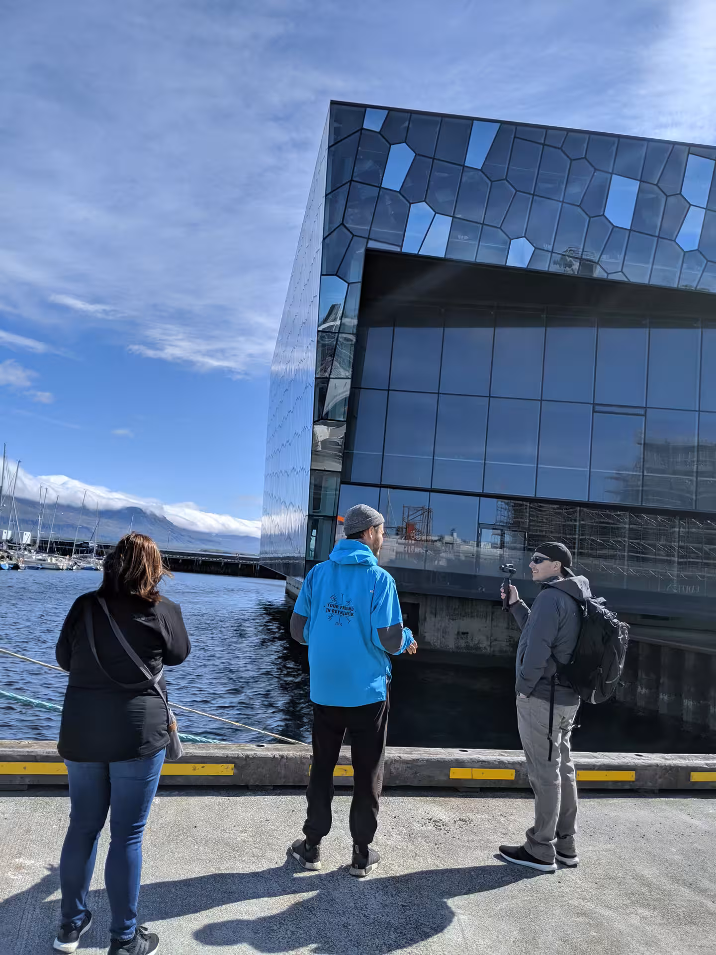 Tour guide in blue jacket leading a small group outside Harpa Concert Hall by Reykjavik harbor