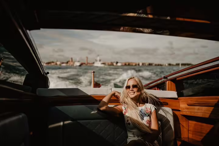 Woman relaxes on a private water taxi ride in Venice, enjoying scenic views and capturing moments with a photographer.