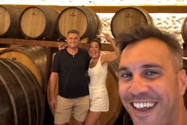 Guests smile among oak barrels during private winery tour and wine museum tasting with local snacks