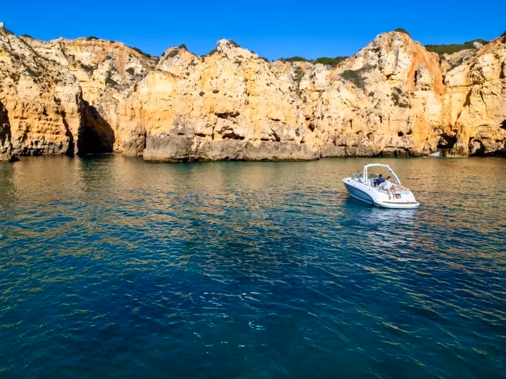 Private yacht charter from Lagos sailing near stunning golden limestone cliffs and crystal-clear turquoise waters of the Algarve coastline.