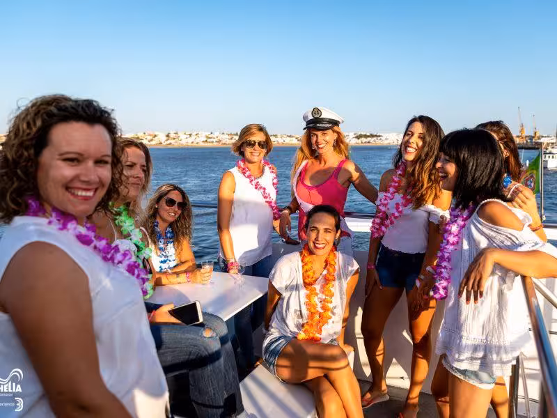 Friends wearing leis on a private Algarve yacht, relaxing on deck and toasting during a sunny group celebration at sea