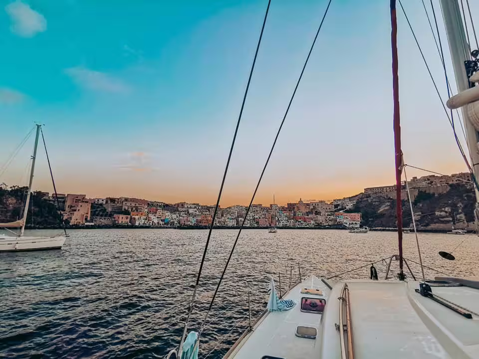 Colorful Procida harbor seen from a catamaran at sunset, showcasing pastel houses, sea cliffs and Tyrrhenian Sea views