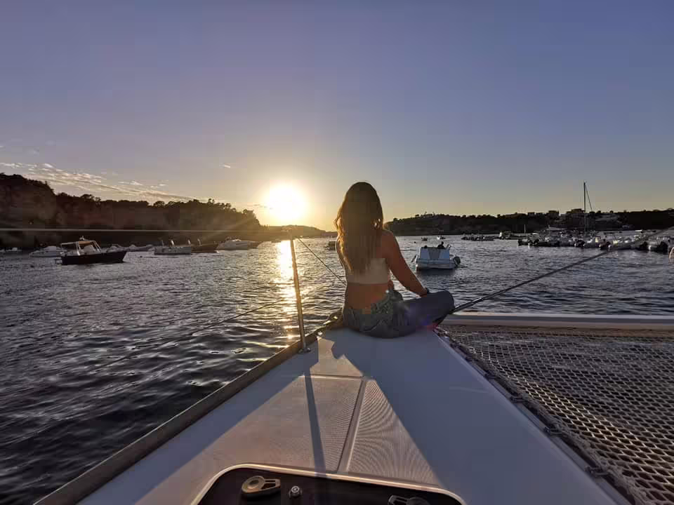 Traveler relaxing on the bow of a catamaran at sunset near Procida, enjoying a scenic boat tour with anchored yachts around