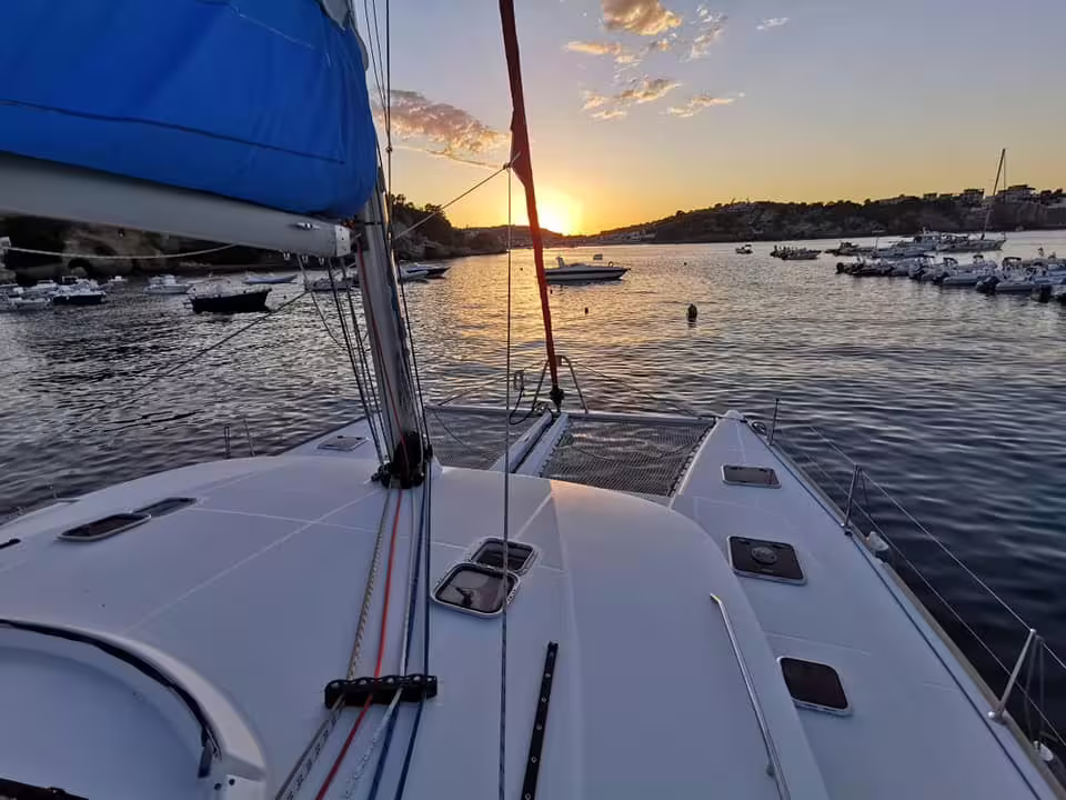 Sunset cruise to Procida by catamaran, sailing past anchored boats and rocky coastline on a serene Mediterranean evening