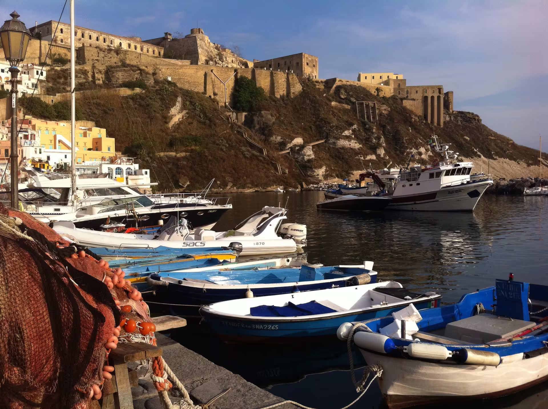 Fishing boats moored below the historic fortress of Procida island, showcasing the harbor stop on a Naples day tour