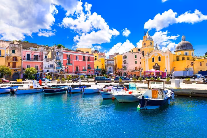 Colorful boats docked at the vibrant waterfront of Procida Island, showcasing its picturesque architecture under a clear blue sky.