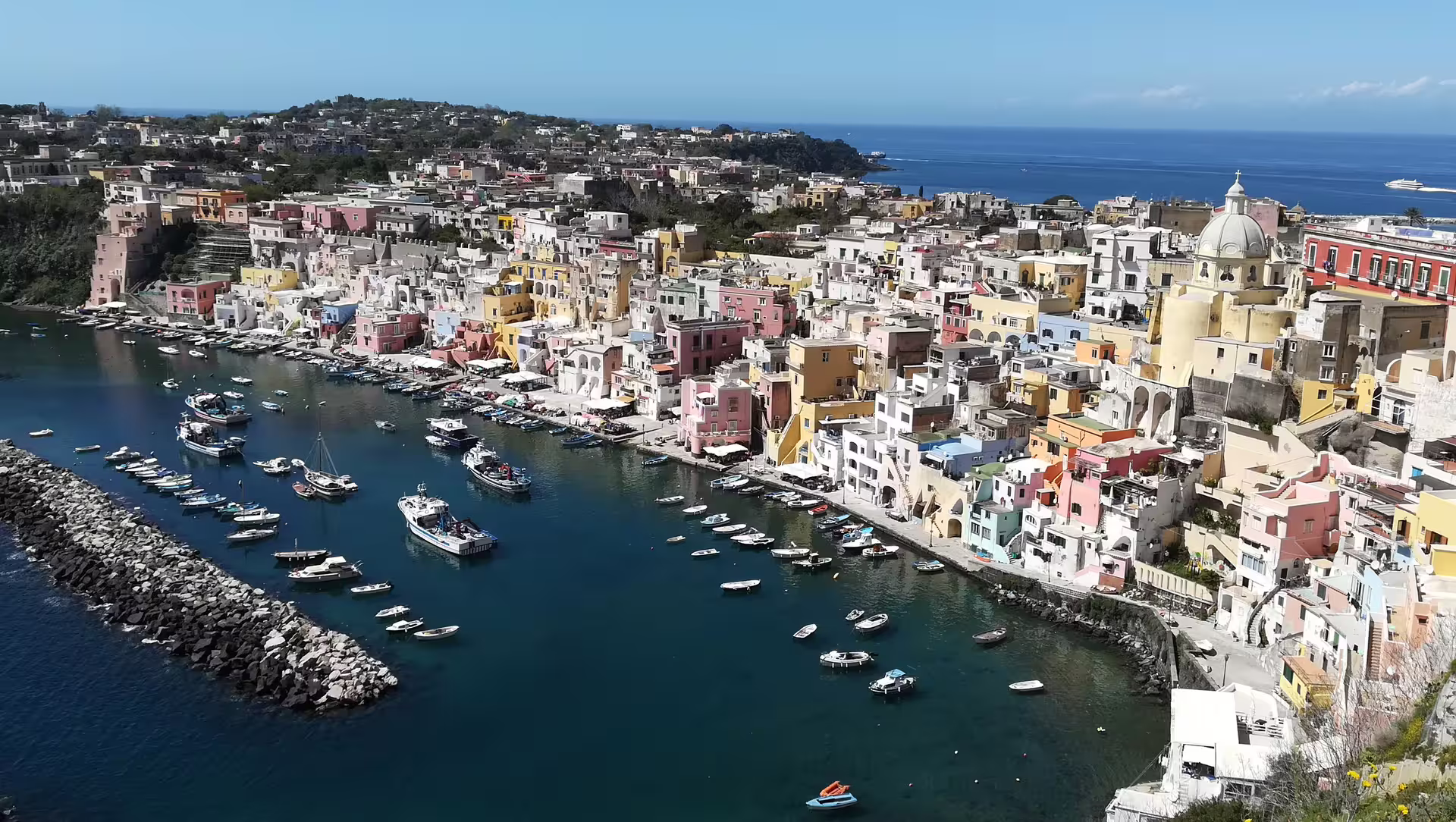 Aerial view of Procida’s colorful Marina Corricella, pastel houses and fishing boats on a sunny Italy day tour excursion
