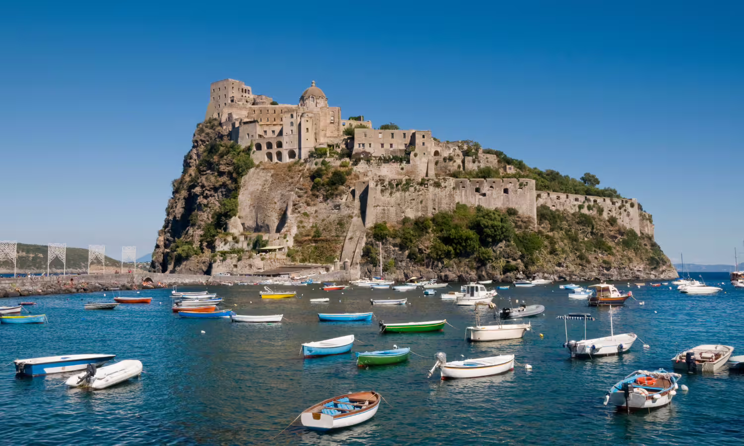 View of Aragonese Castle on Ischia with colorful boats in the bay, seen during a Procida VIP catamaran day trip