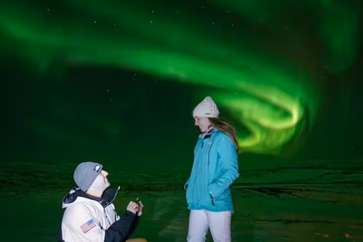 Man proposing on one knee under vivid green northern lights aurora borealis in Reykjavik Iceland