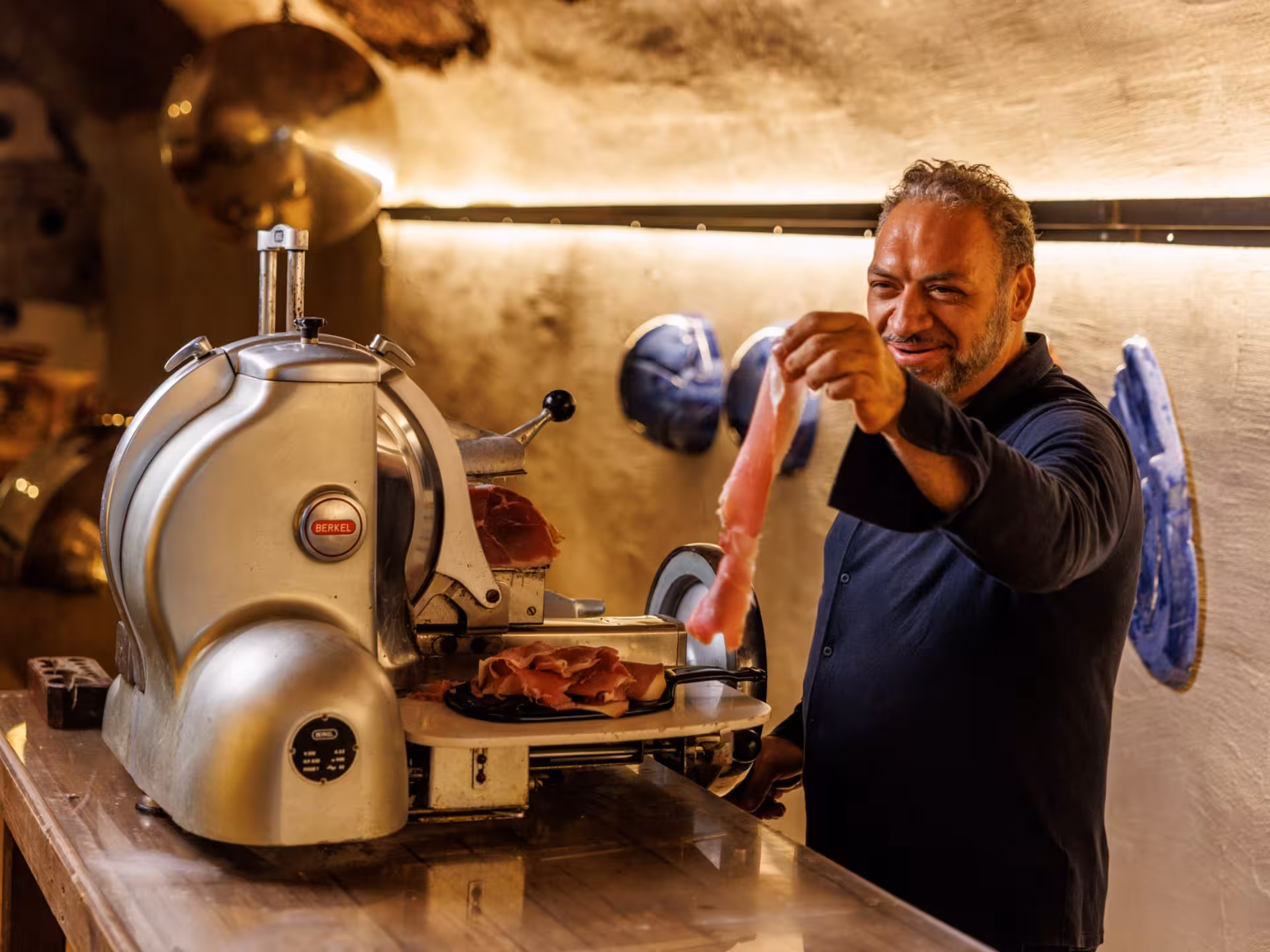 Smiling man presenting sliced prosciutto in a rustic underground cellar in Rome, highlighting Italian food pairing experience.
