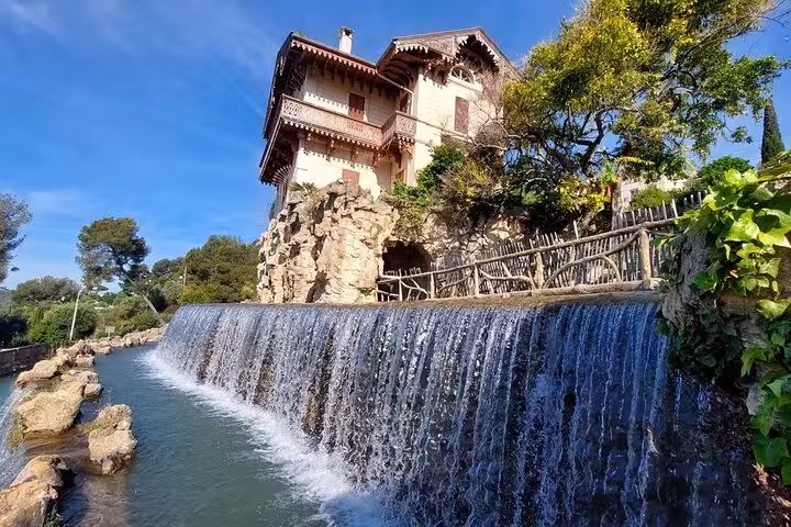 Charming Provencal house by a cascading waterfall, surrounded by lush greenery on a sunny day.