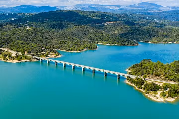 Aerial view of a bridge over a turquoise lake amidst the lush green landscape of the Provencal countryside.