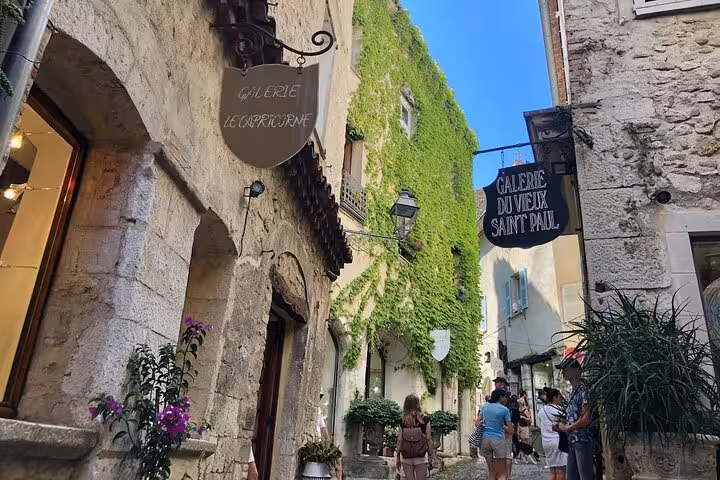 Tourists wandering through picturesque alleyways adorned with lush greenery in a quaint Provencal village.