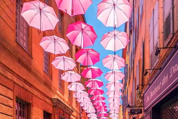 Artistic display of pink umbrellas hanging over a quaint street in a Provencal village, creating a vibrant scene.