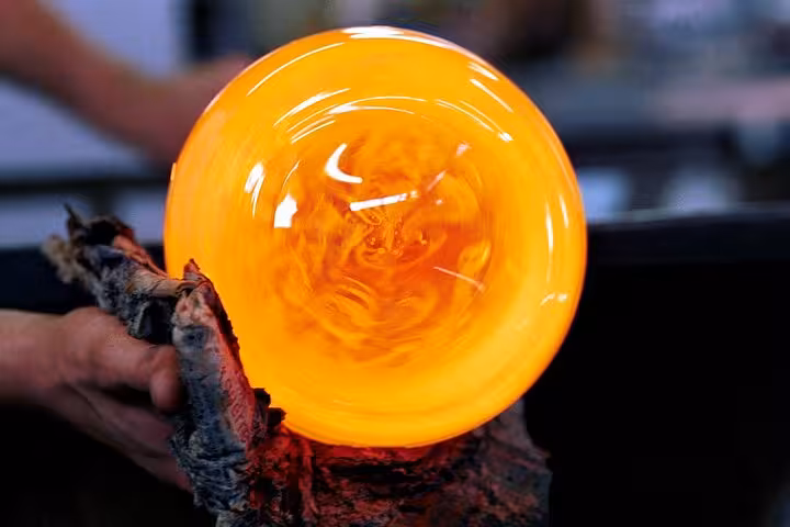 Close-up of a glowing glass orb being shaped by an artisan in a Provence countryside workshop, showcasing local craftsmanship.
