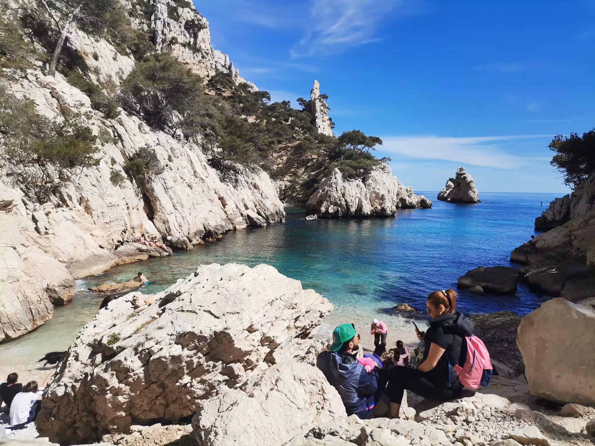 Rest stop at a turquoise Calanques cove in Provence, France, with hikers by white cliffs and clear water