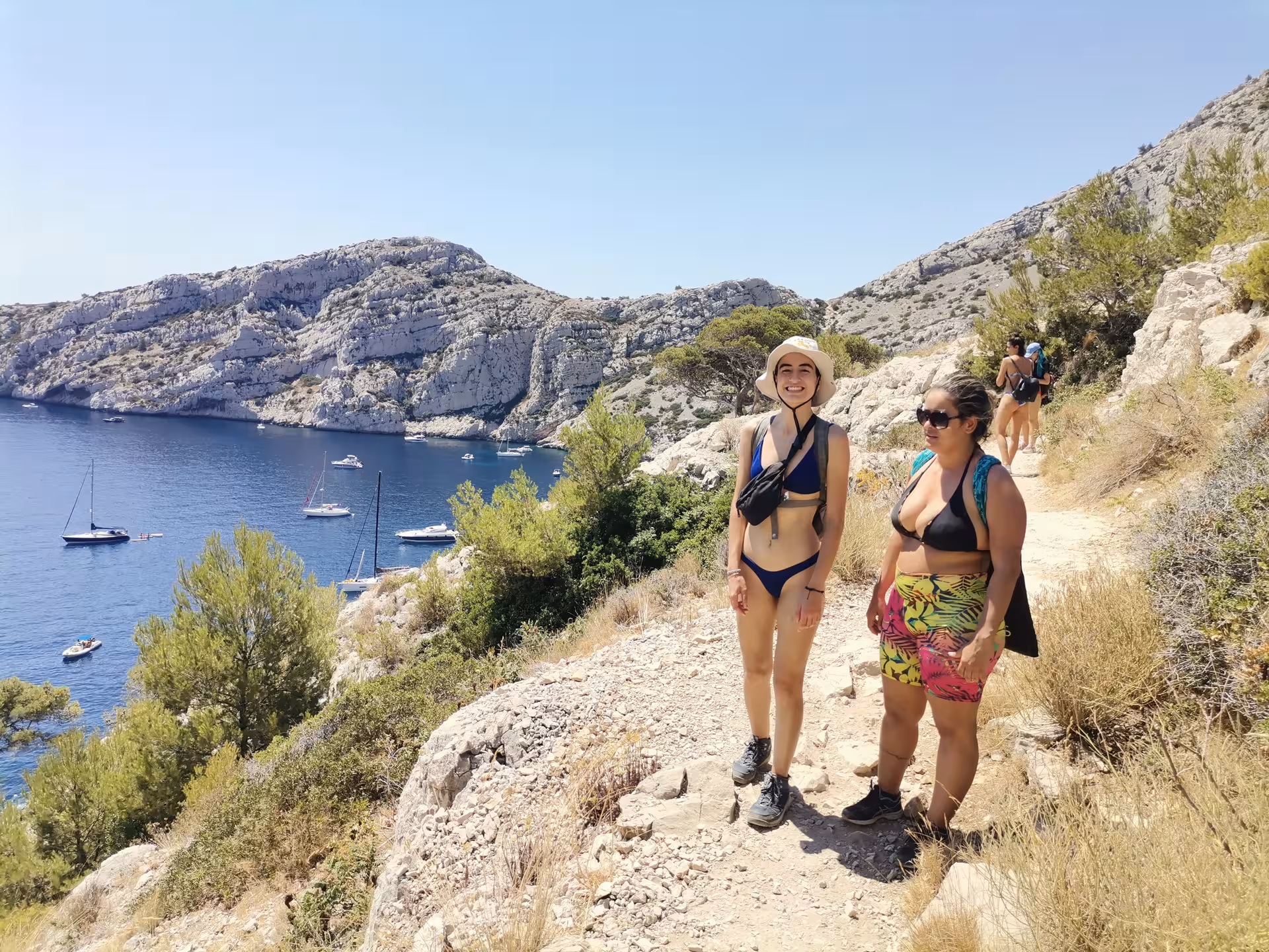 Hikers on a coastal trail above Calanques near Marseille, Provence, with sailboats on turquoise Mediterranean water