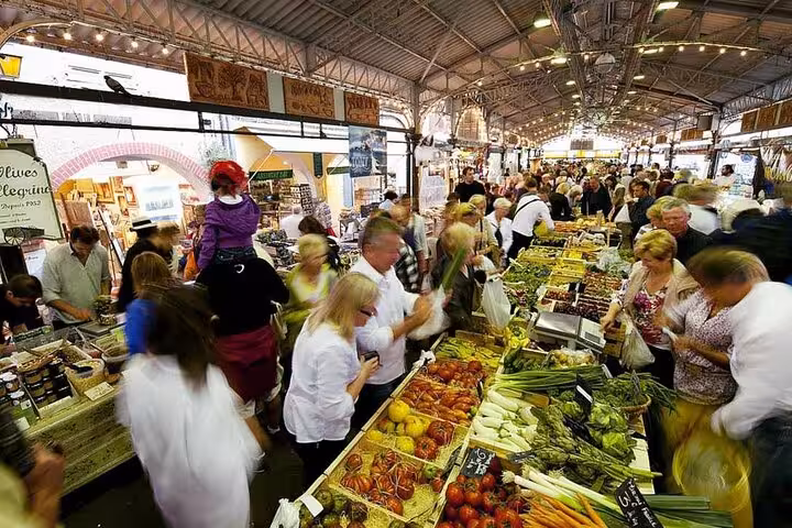 Bustling indoor Provence market with fresh vegetables and crowds of shoppers along vendor stalls