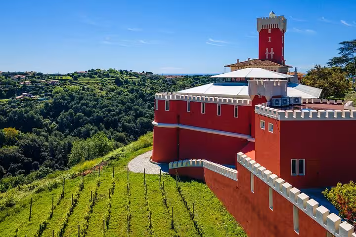 Scenic view of a vibrant red castle overlooking lush vineyards and rolling hills in the Provencal countryside.