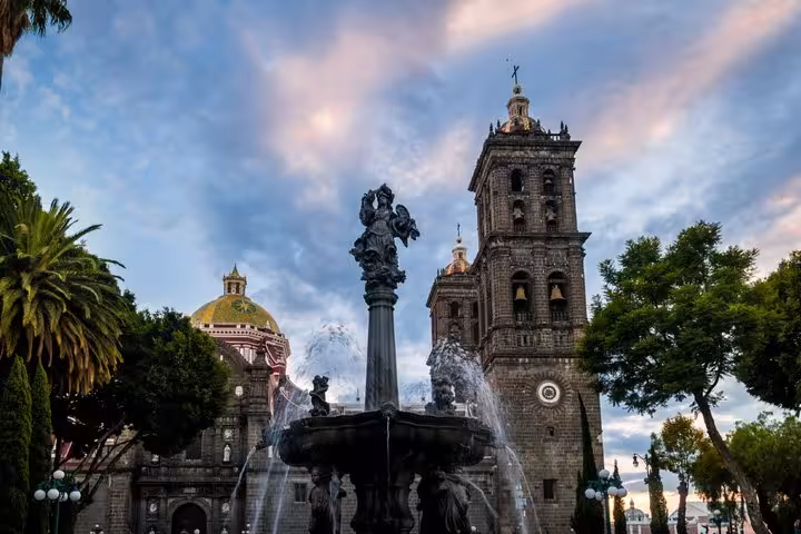 Ornate fountain in front of Puebla Cathedral tower and golden dome at dusk