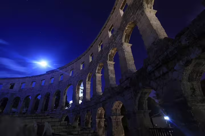 Night view of Pula Arena amphitheater arches under moonlight in Pula, Croatia, with skip-the-line entry