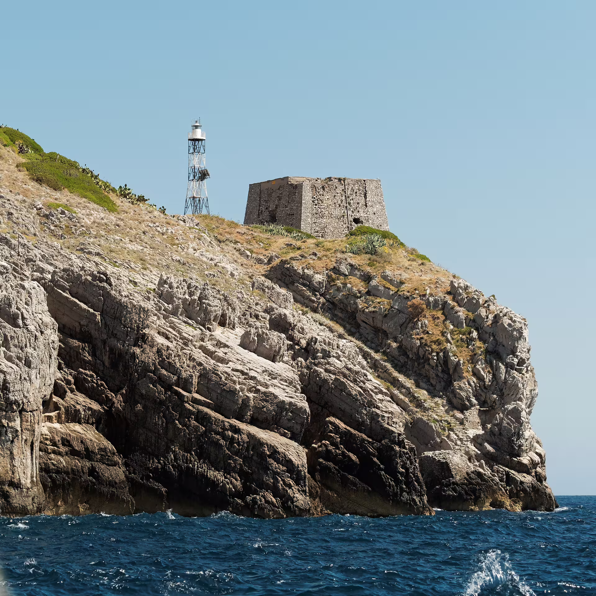 Rocky Punta Campanella headland with historic watchtower and metal lighthouse rising above the blue Tyrrhenian Sea