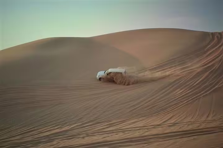 White 4x4 SUV powerfully dune bashing across sandy Qatar desert slopes kicking up dust