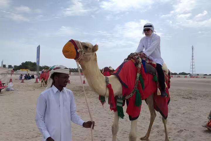 Tourist riding a decorated camel with a guide during Qatar desert safari camel ride experience