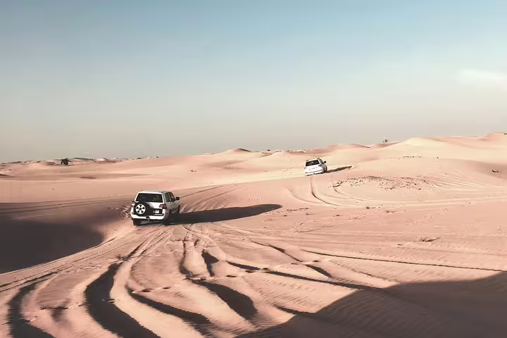 Two 4x4 SUVs dune bashing across vast Qatar desert sand dunes on an thrilling off-road safari tour