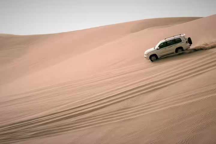 4x4 SUV dune bashing across vast golden sand dunes during an exhilarating Qatar desert safari experience