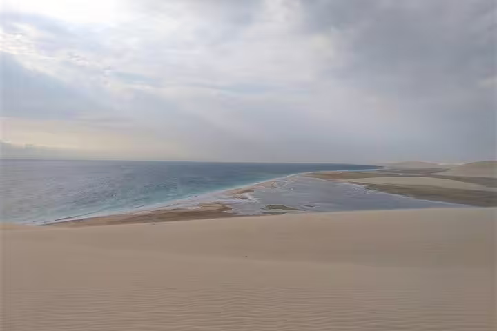 Stunning Qatar desert landscape with golden sand dunes meeting the turquoise sea under cloudy skies