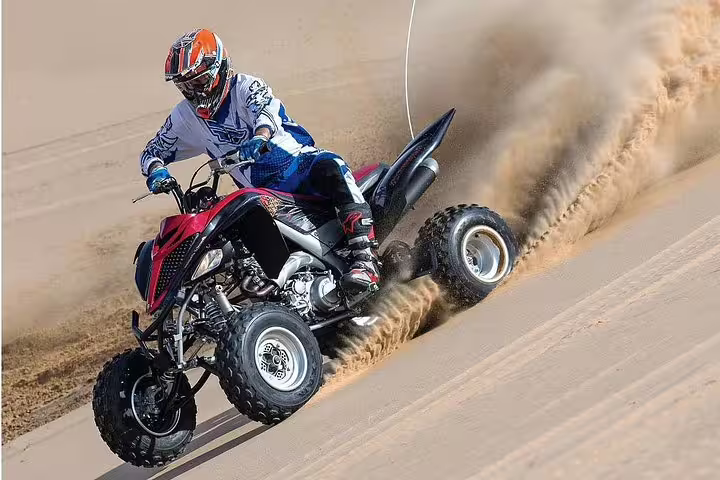 Thrilling quad bike ride on Qatar desert sand dunes kicking up dust during an exciting safari adventure