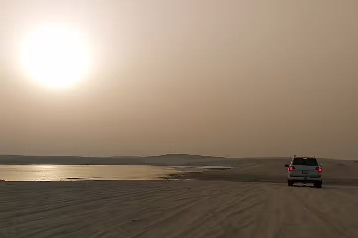 SUV driving along Qatar desert shoreline at golden sunset during an exclusive guided safari tour