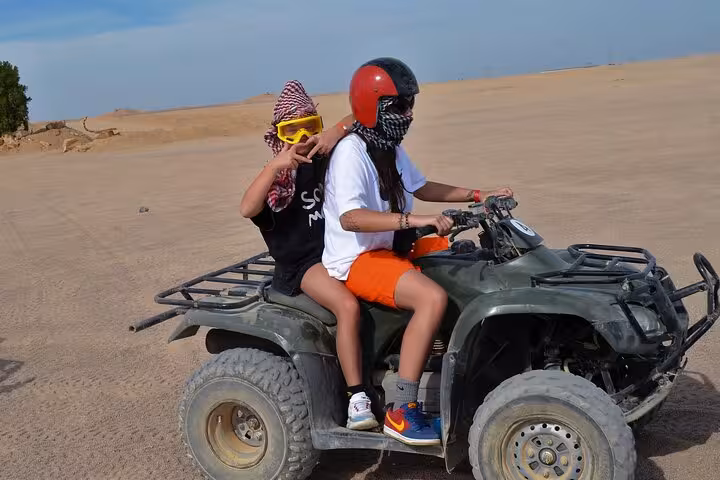 Two riders on an ATV quad in Sharm El Sheikh desert wearing helmets and goggles on a sunrise or sunset safari