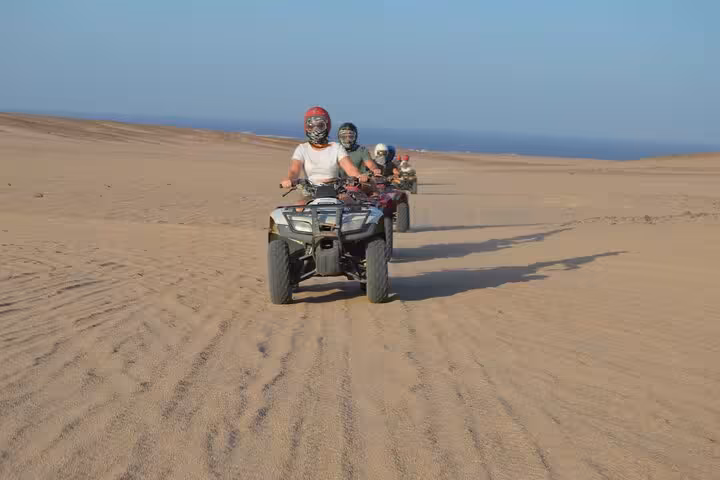 Group ATV quad biking across Sharm El Sheikh sand dunes near the sea, sunrise or sunset desert adventure