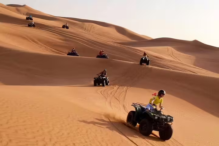 Group of tourists riding quad bikes across expansive desert dunes on a guided self-drive adventure.