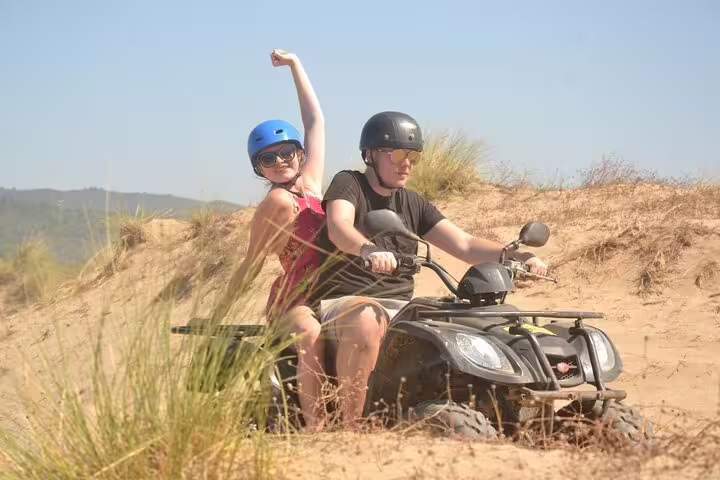 Couple on a quad bike exploring sandy dunes under a clear blue sky near Kusadasi Port.