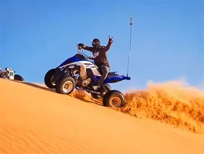 Adventurer rides quad bike on golden sand dunes in Merzouga Erg Chebbi Desert under clear blue sky.